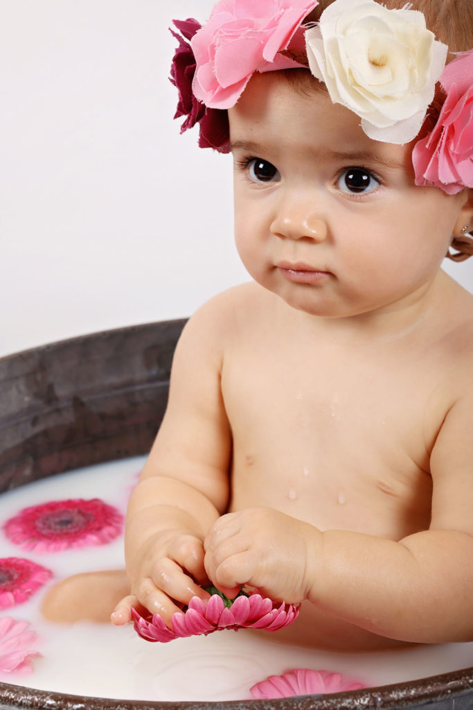 Bébé fille dans une baignoire de zinc qui prend un bain de lait avec des fleurs
