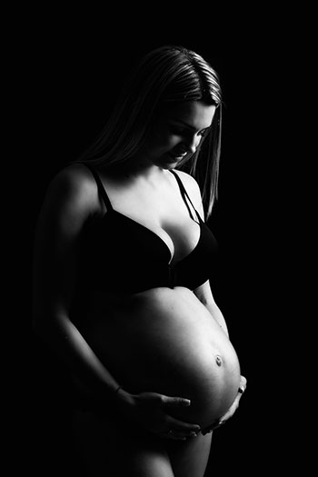 Photo artistique de femme enceinte en noir et blanc, elle soutien son ventre avec ses deux mins et regarde son future bébé avec tendresse et amour. photographe specialisée en photographie de grossesse en noir et blanc. 