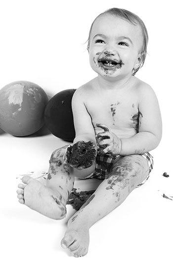 Photographie d'un smash cake en noir et blanc, un garçon d'un an qui découvre pour la première fois le gâteau de chocolat. 