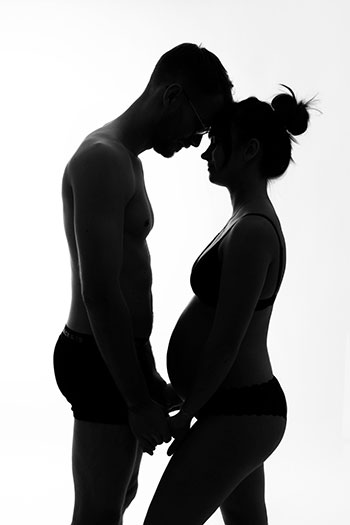 Photo contrastée en noir et blanc d'un couple de profil à la caméra, ils se tient par les mains et ses fronts sont collées.  